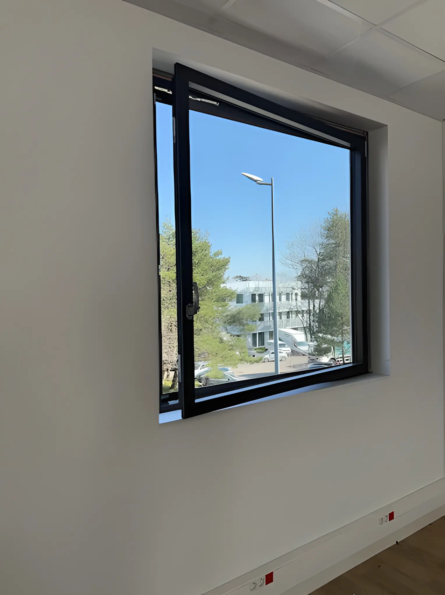 Fenêtre aluminium noire ouverte en soufflet dans un bureau aux murs blancs