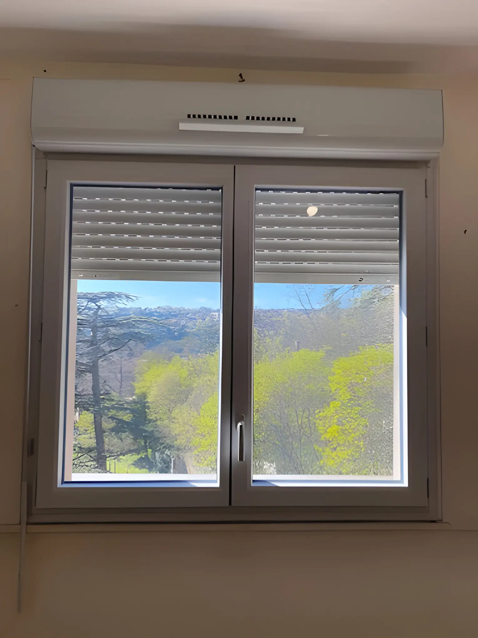 Fenêtre blanche deux vantaux et son volet roulant, coffre à entrée d’air, vue de l’intérieur
