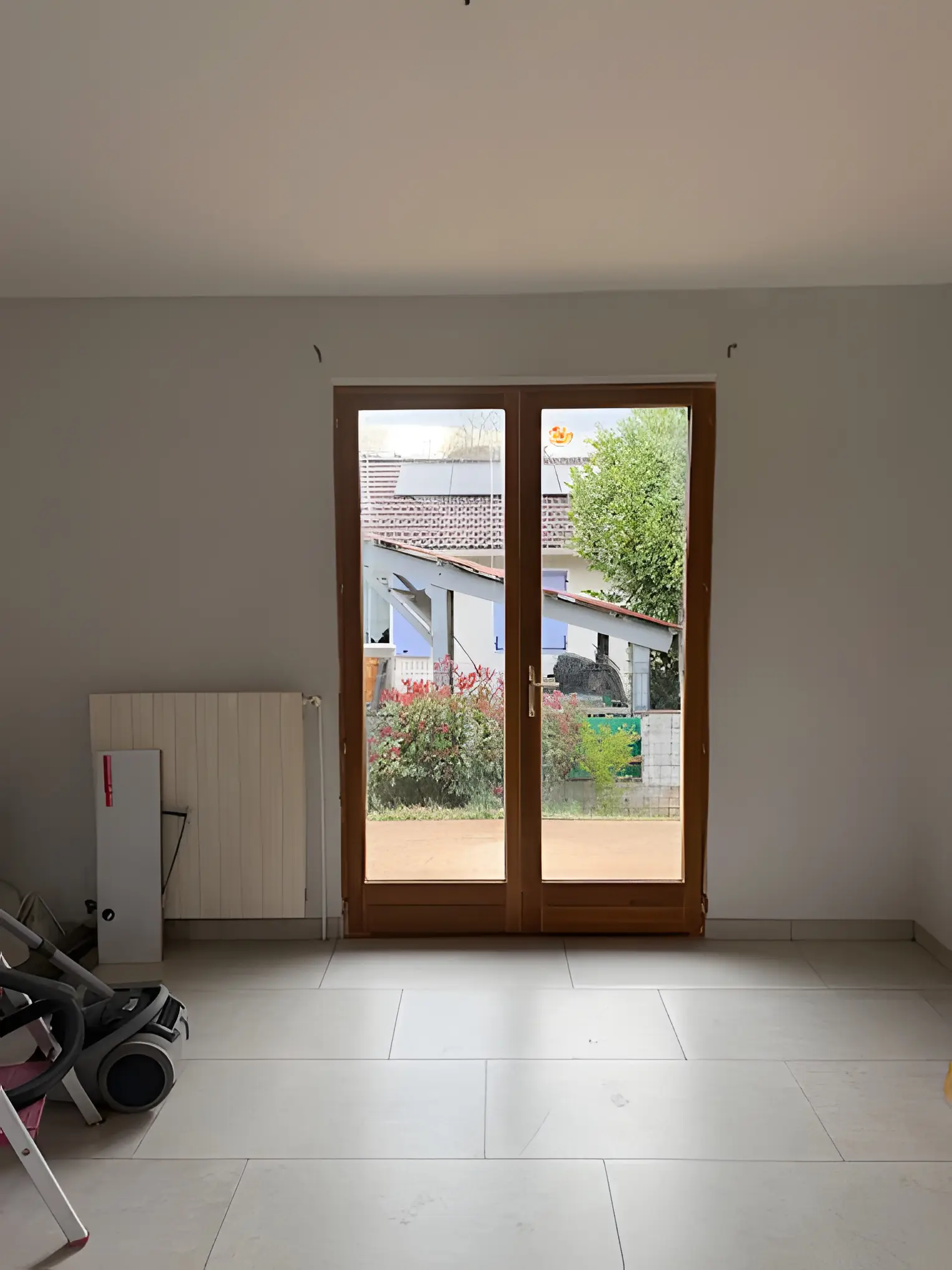 Porte-fenêtre deux vantaux ton bois dans une pièce en travaux, ouverte sur le jardin